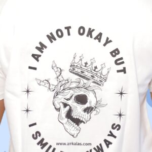 A crowned skull with a twisted smile and shattered expression beneath the words “I AM NOT OKAY BUT I SMILE ANYWAYS,” symbolizing the bold defiance of pain with deadly grace. Dark, raw, and unbreakably royal.