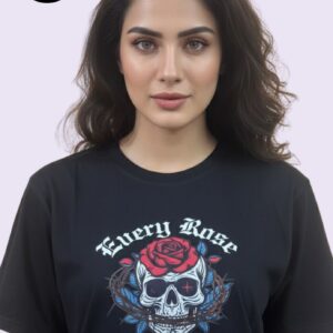 A woman stands gracefully wearing a black T-shirt featuring a striking skull and rose graphic with the words “Every Rose Has Its Thorn” in bold, artistic fonts. The blend of red, blue, and white colors, along with the intricate design of a rose and thorns over the skull, creates a bold yet elegant look. The gentle background of soft drapes highlights both her presence and the edgy T-shirt design, embodying strength and beauty
