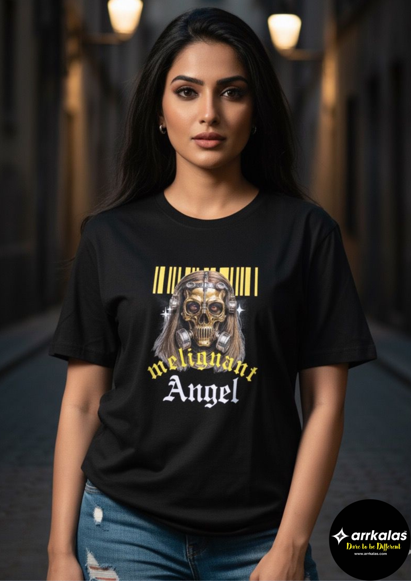 A confident Indian woman stands in an atmospheric urban alley, wearing a black T-shirt featuring a striking design of a golden skull with long hair, metal details, and a barcode above, with bold text reading “malignant Angel” in yellow and white gothic fonts, blending edgy style with urban elegance